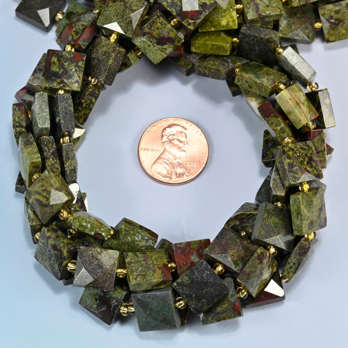 Natural dragon blood stone faceted flat square beads 10x10mm coiled in a loop around a US penny for scale, close-up of the faceted flat square shape