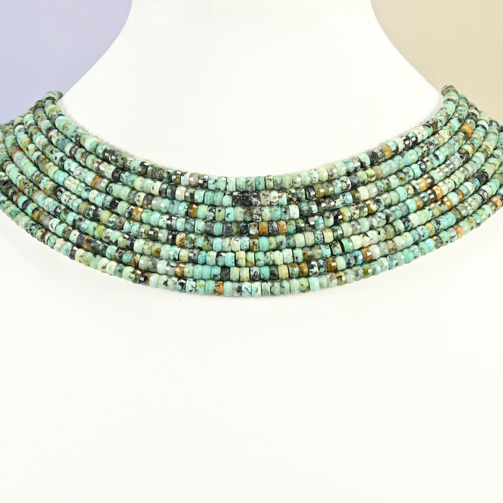 African howlite faceted heishi disc strands arranged as a layered collar on a white display bust, green beads across the neck