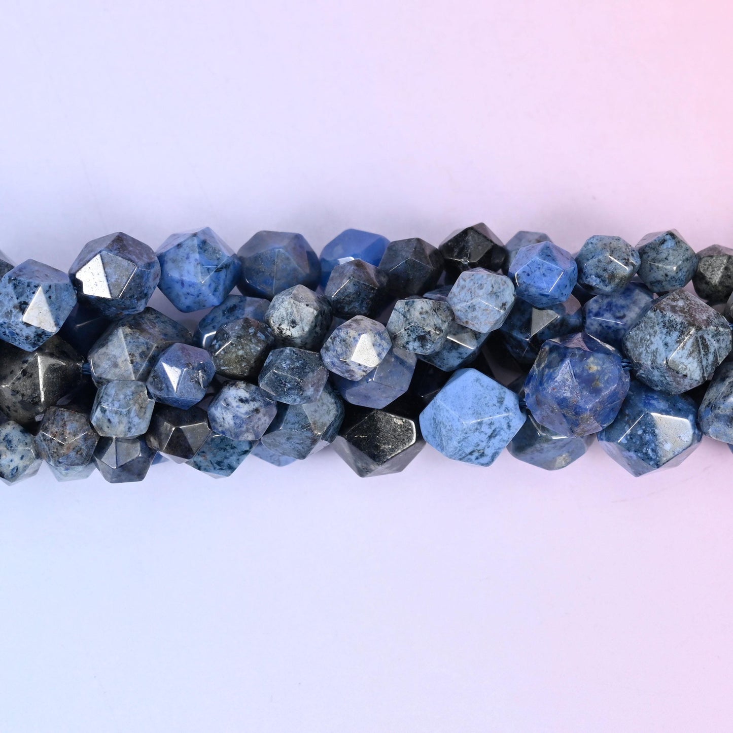 Denim and ink blue clouded with charcoal grey and pale speckling, cut in a diamond star pattern so flat triangular facets throw crisp silver-white points across an otherwise deep, mottled stone.