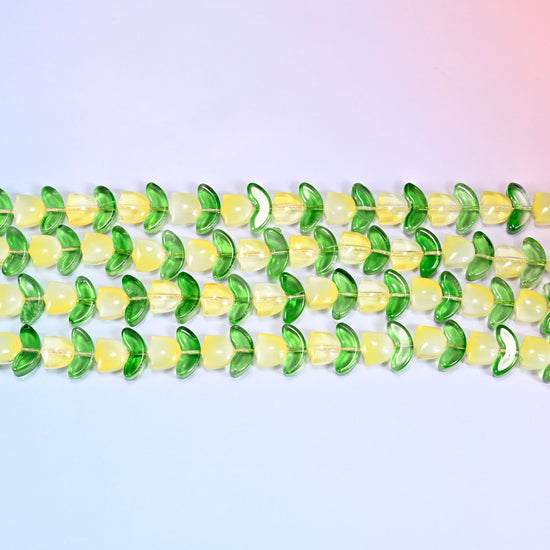 Close-up macro view of yellow tulip and green leaf glass beads in a dense repeating row pattern on a lavender and pink gradient background.
