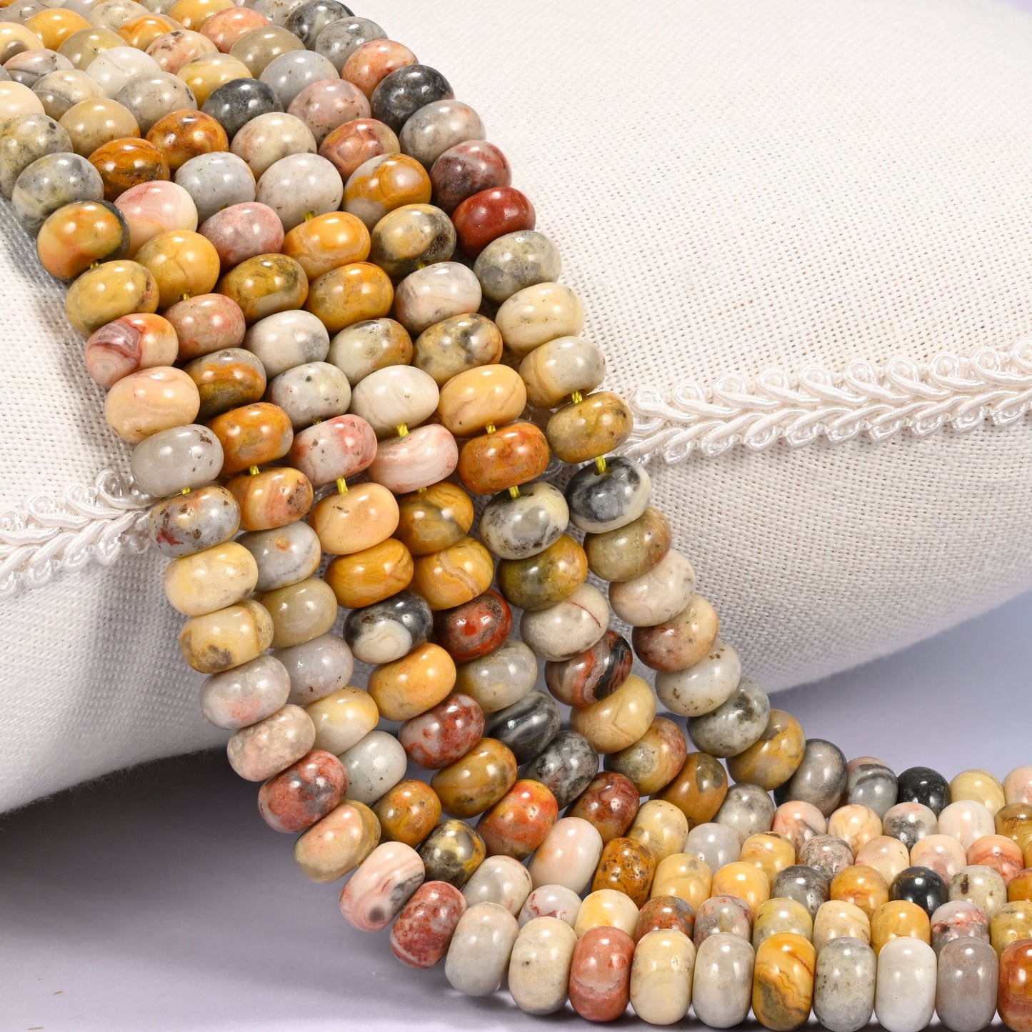 Close-up of multiple strands of polished Crazy Agate rondelle beads in mustard, gray, and rust tones, draped over a cream fabric jewelry display bust.