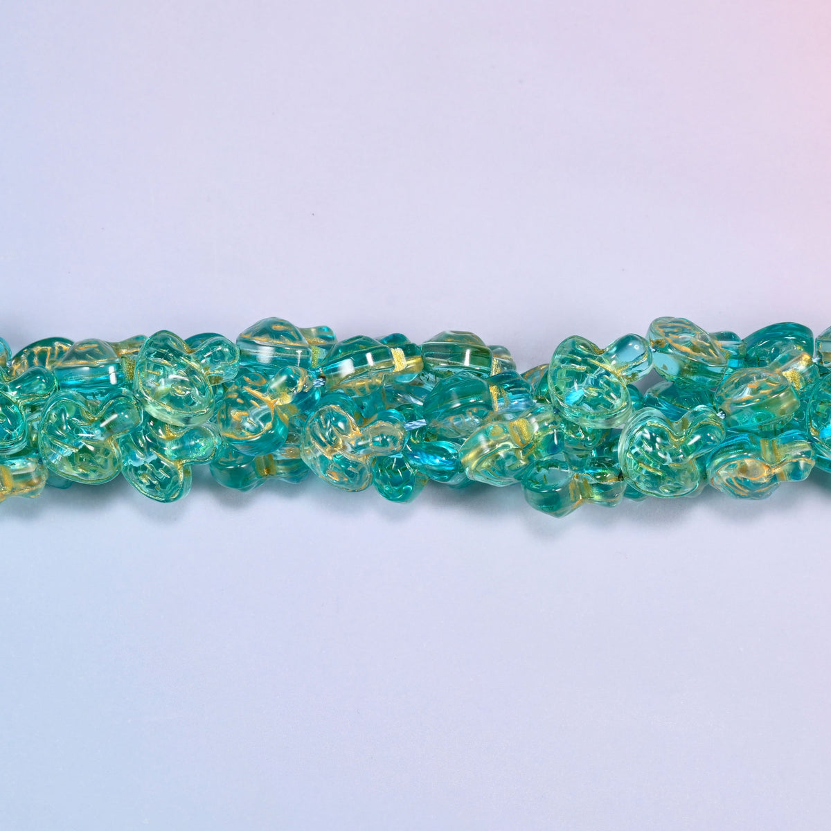 Aqua gold flat mushroom glass beads, domed caps over short stems, strands laid in a gentle wave straight across the frame.