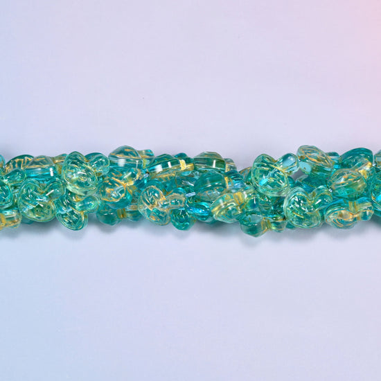 Aqua gold flat mushroom glass beads, domed caps over short stems, strands laid in a gentle wave straight across the frame.