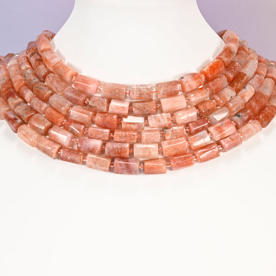 Multi-strand Golden Strawberry Quartz faceted tube bead necklace laid flat on a mannequin neck form against a lavender background.