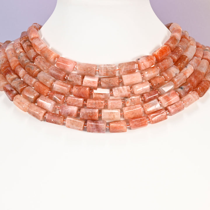 Multi-strand Golden Strawberry Quartz faceted tube bead necklace laid flat on a mannequin neck form against a lavender background.