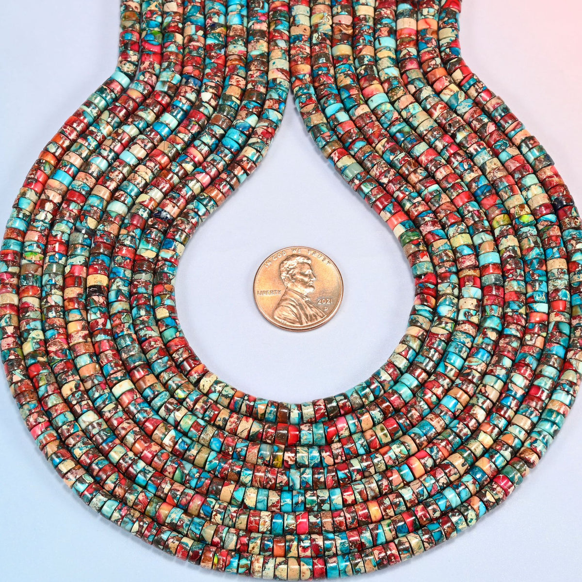 Dyed red blue sea sediment jasper heishi disc strands formed into a teardrop loop around a US penny for scale