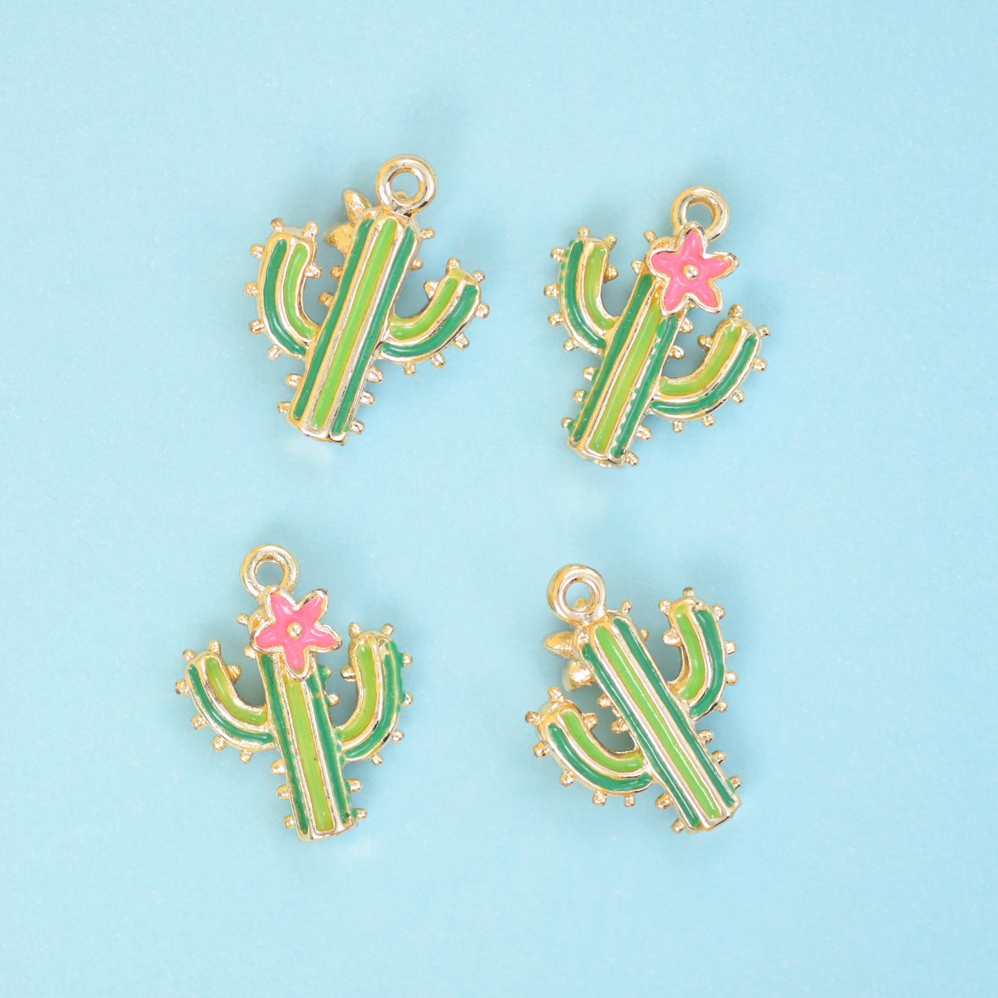 A chunky saguaro in two-tone green enamel, outlined and dotted in warm gold filled brass and topped with a small pink…