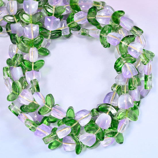 Horizontal row of lavender tulip and green leaf glass beads laid straight across a lavender background, showing the alternating flower and leaf pattern.