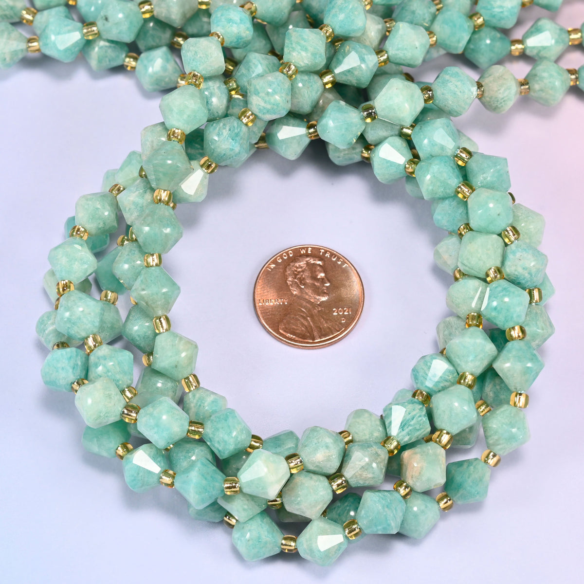 Green Amazonite faceted bicone beads 8mm with gold-tone spacers, strand coiled with a penny centered, close-up of the beads