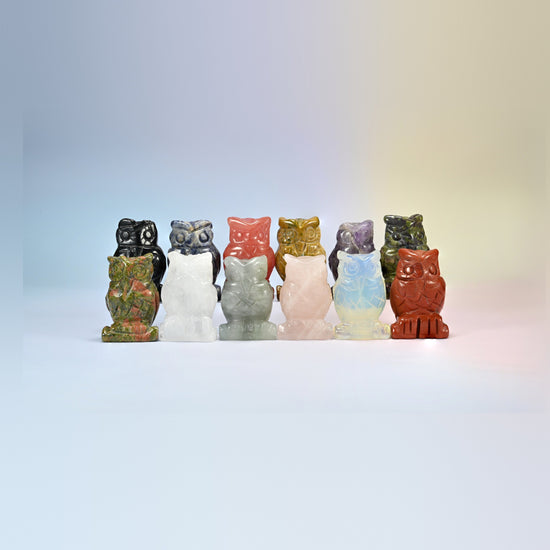 Row of owl crystal carvings in black obsidian, amethyst, red jasper, tiger eye, rose quartz, opalite and more