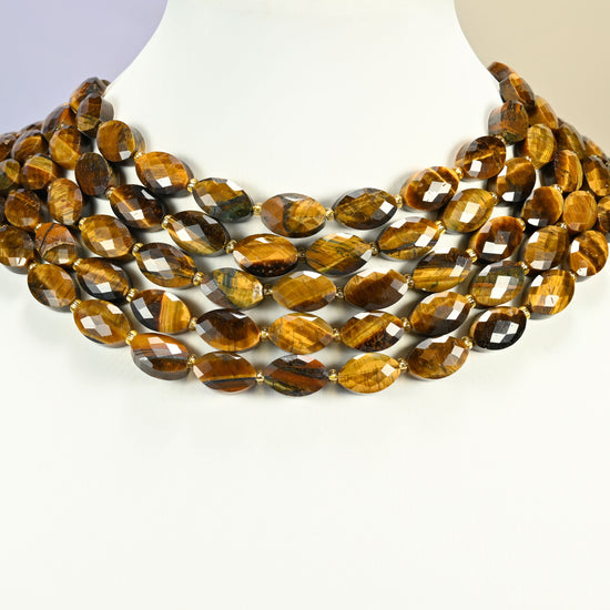 Tiger eye faceted flat oval strands arranged as a layered collar on a white display bust, golden brown beads across the neck