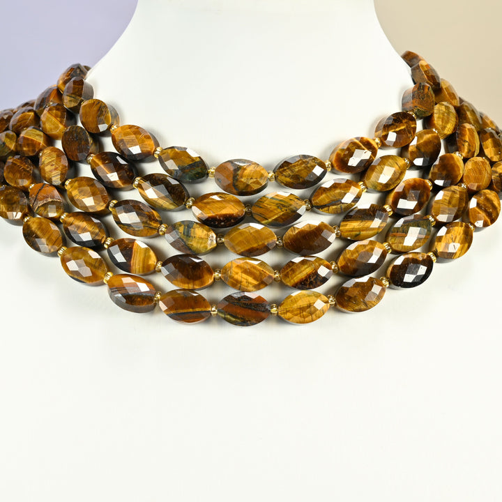 Tiger eye faceted flat oval strands arranged as a layered collar on a white display bust, golden brown beads across the neck