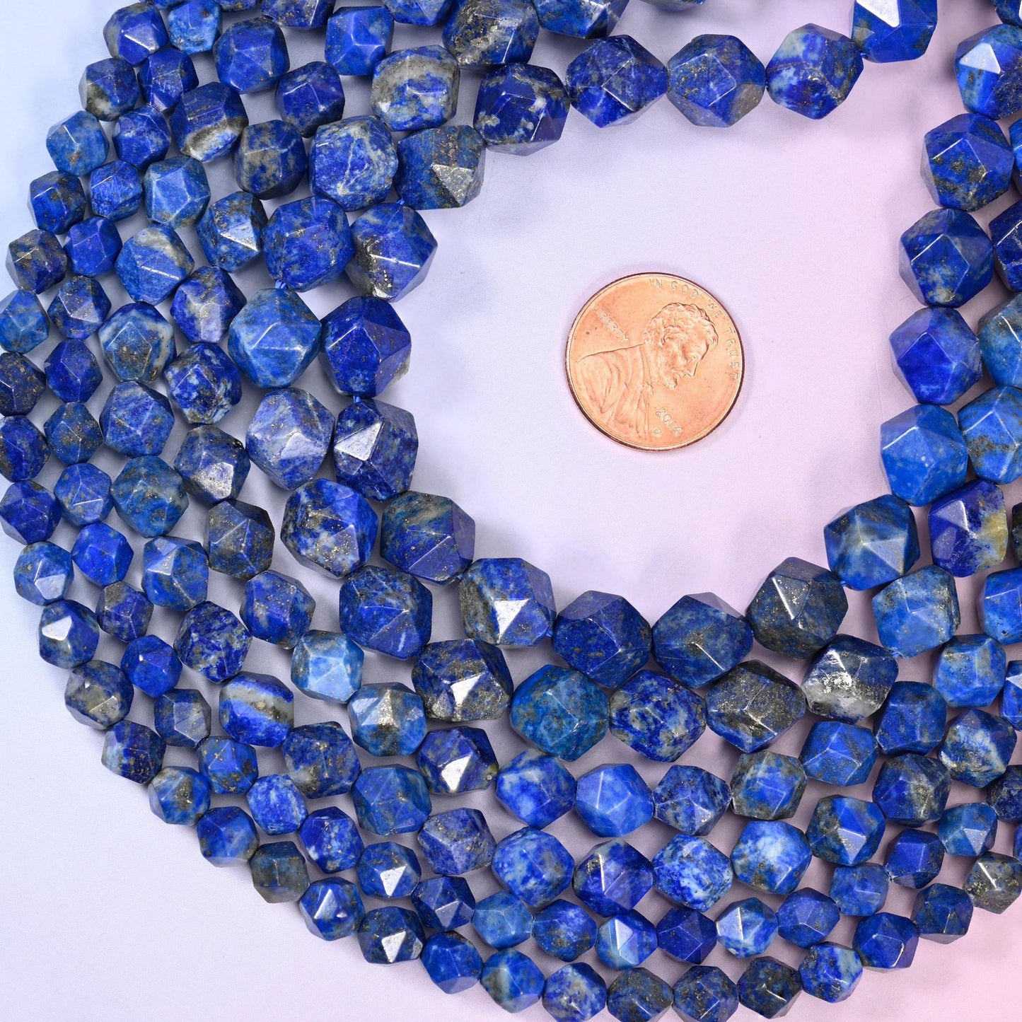 Blue Lapis Lazuli diamond star cut beads coiled around a US penny for size reference, centre drilled with a polished faceted finish