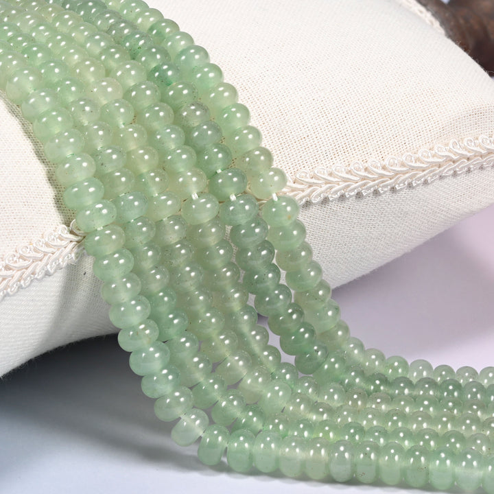 Green Aventurine gemstone rondelle beads draped in rows over a cushion, smooth polished light green discs on 15.5 inch strands