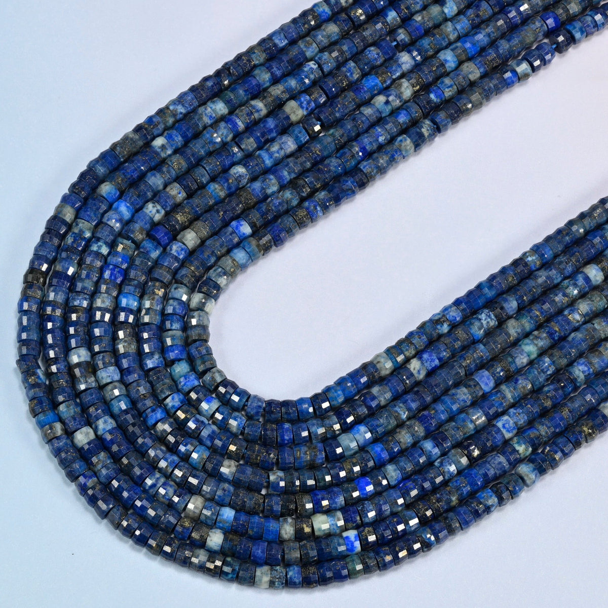 Dark blue lapis faceted heishi disc beads in several strands curved into a wide U, deep dark blue stone with gold flecks