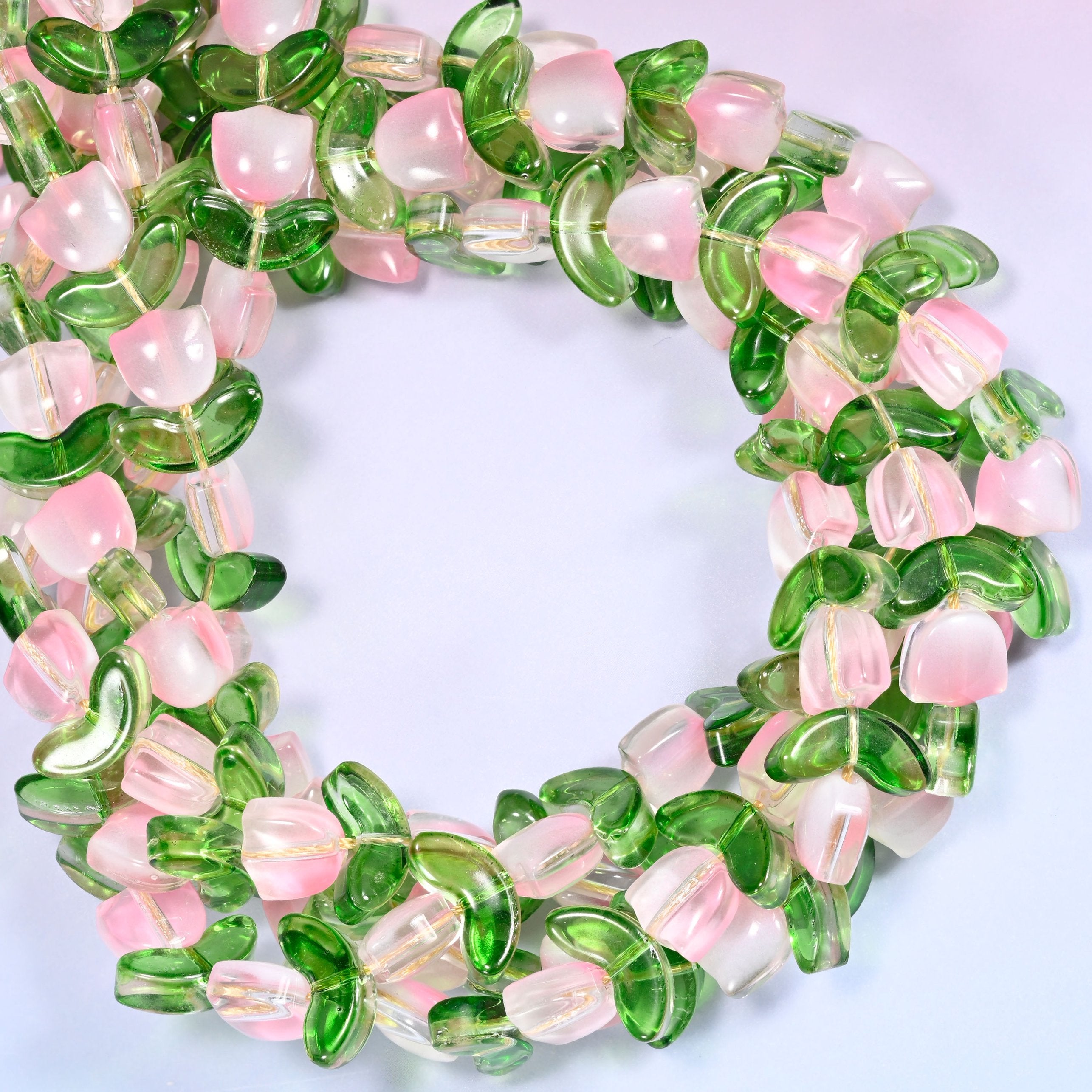 Wide circular coil of pink tulip and green leaf glass bead strands on a lavender background, showing the full wreath shape.