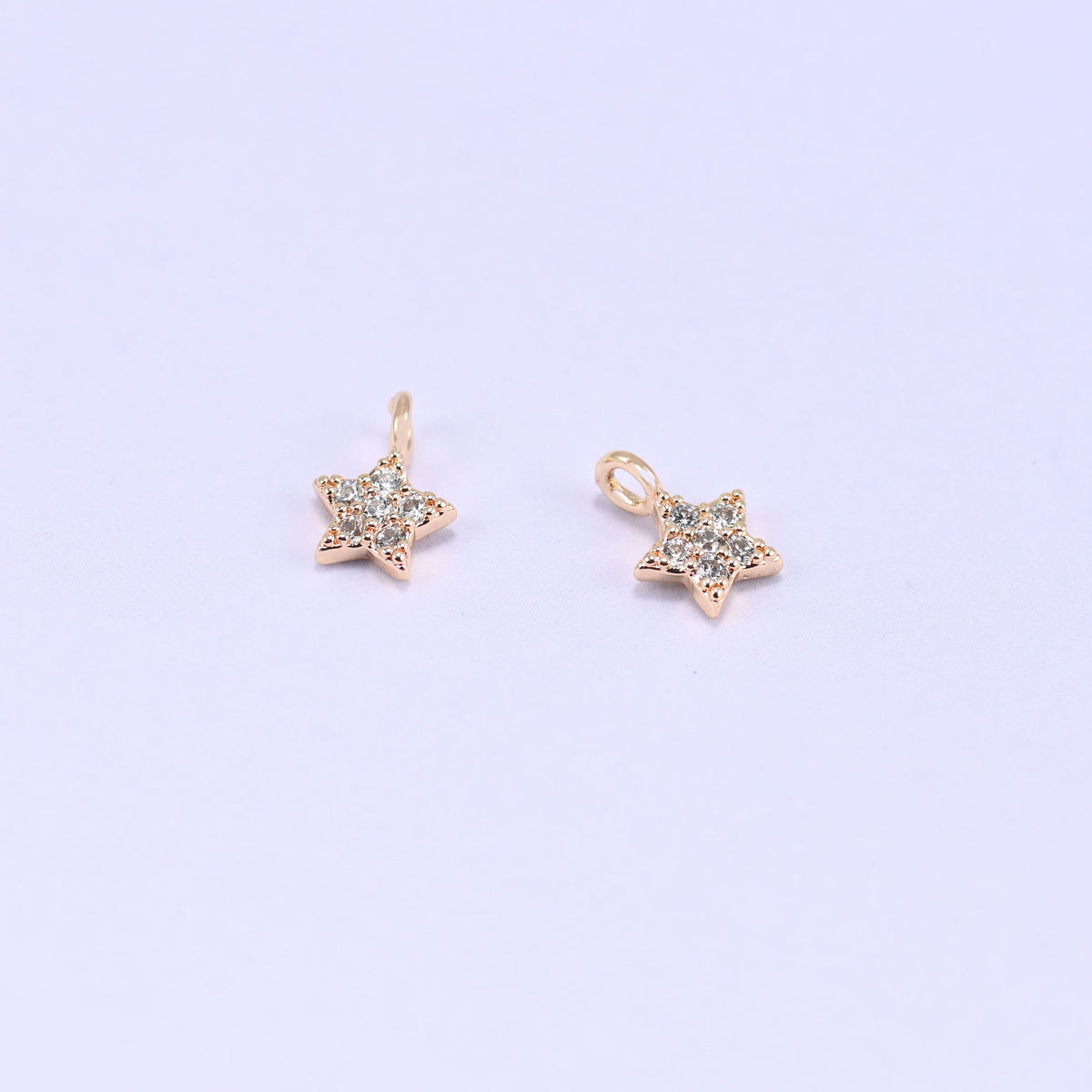Small gold charms, two star charms with clear cubic zirconia shown close up