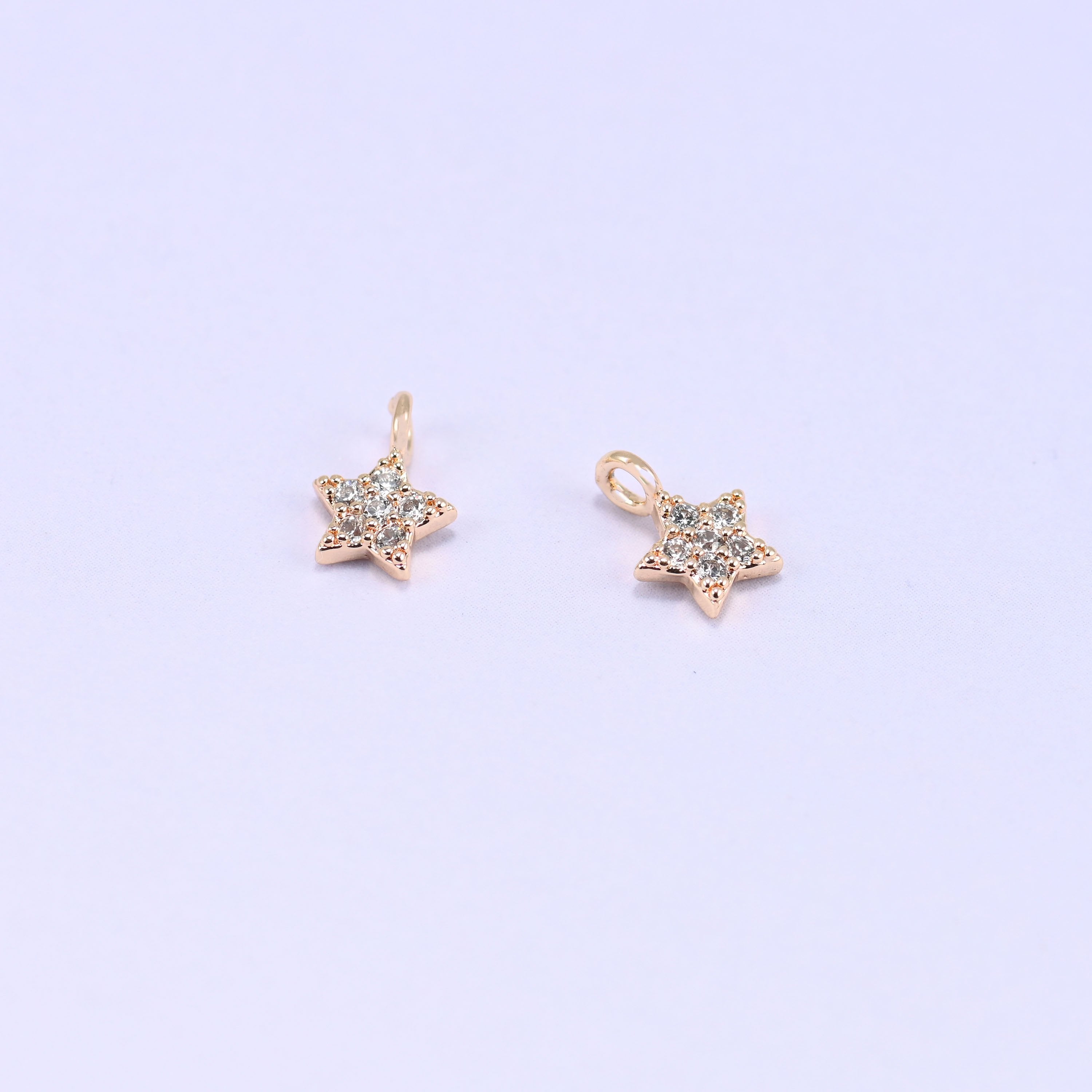 Small gold charms, two star charms with clear cubic zirconia shown close up