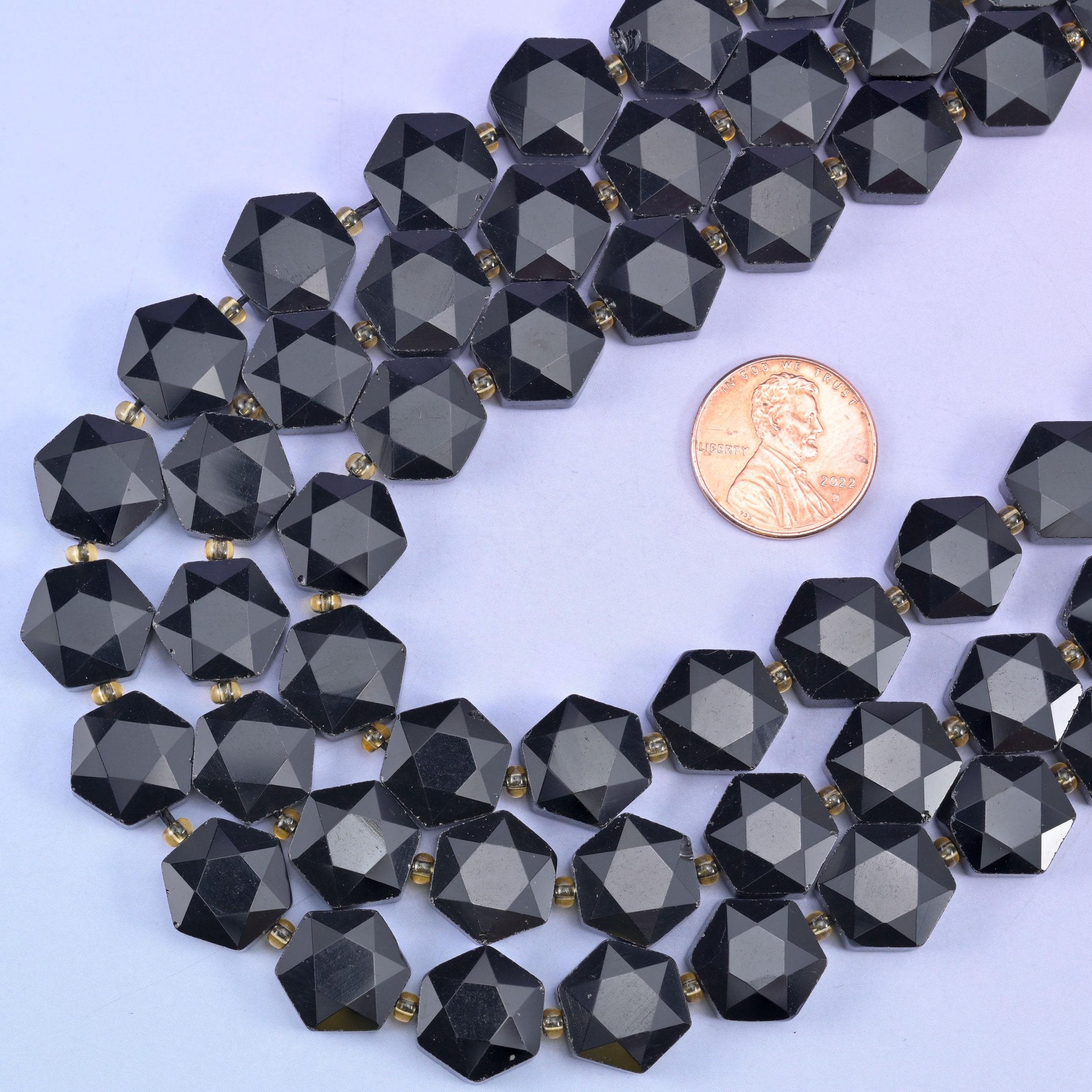 Obsidian hexagon beads looped beside a US penny for a clear sense of the 12mm size