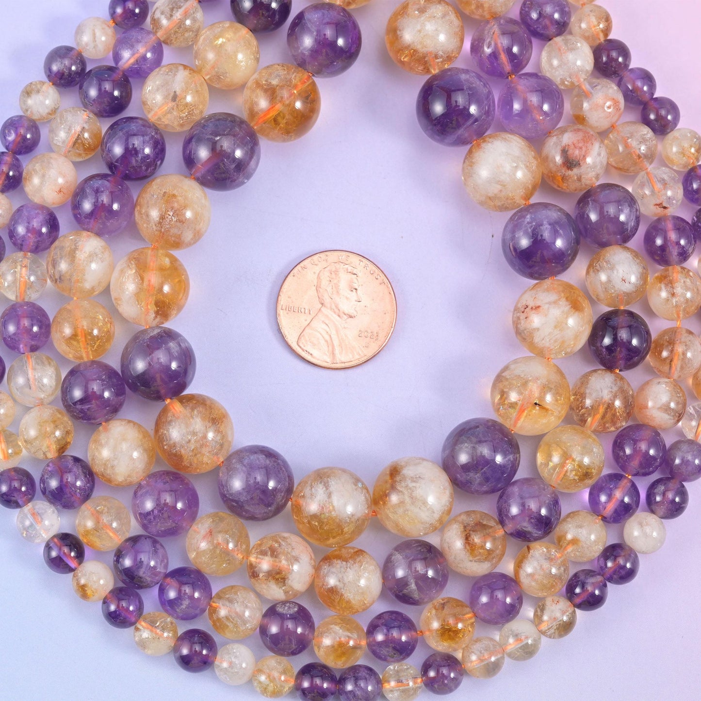Two quartzes on one strand: deep grape purple amethyst next to warm champagne citrine, both translucent with faint white veils and inclusions drifting through them, polished to a clear glassy round.