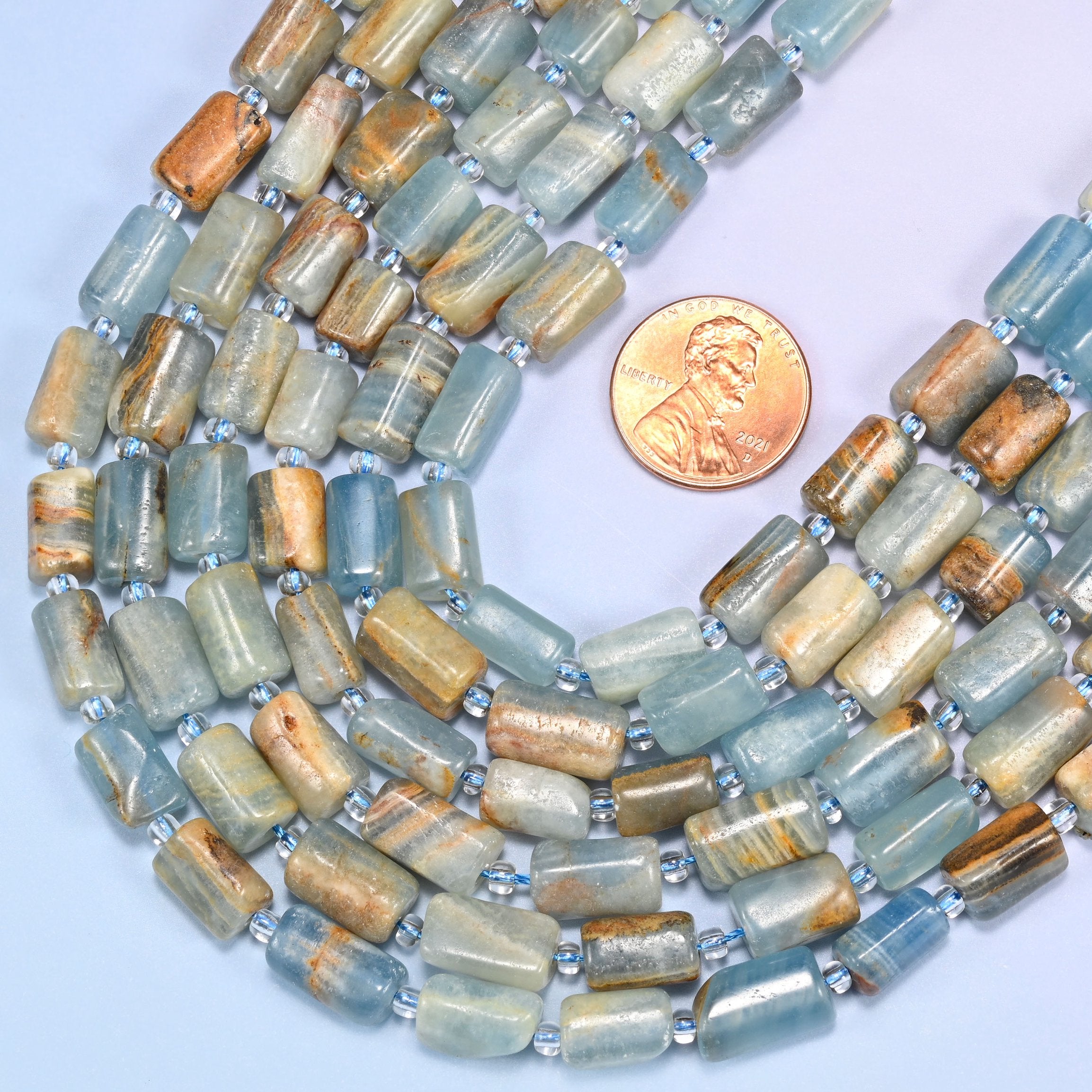 Rows of faceted Blue Calcite tube beads laid straight on a lavender surface, showing the range of natural blue and tan coloring.