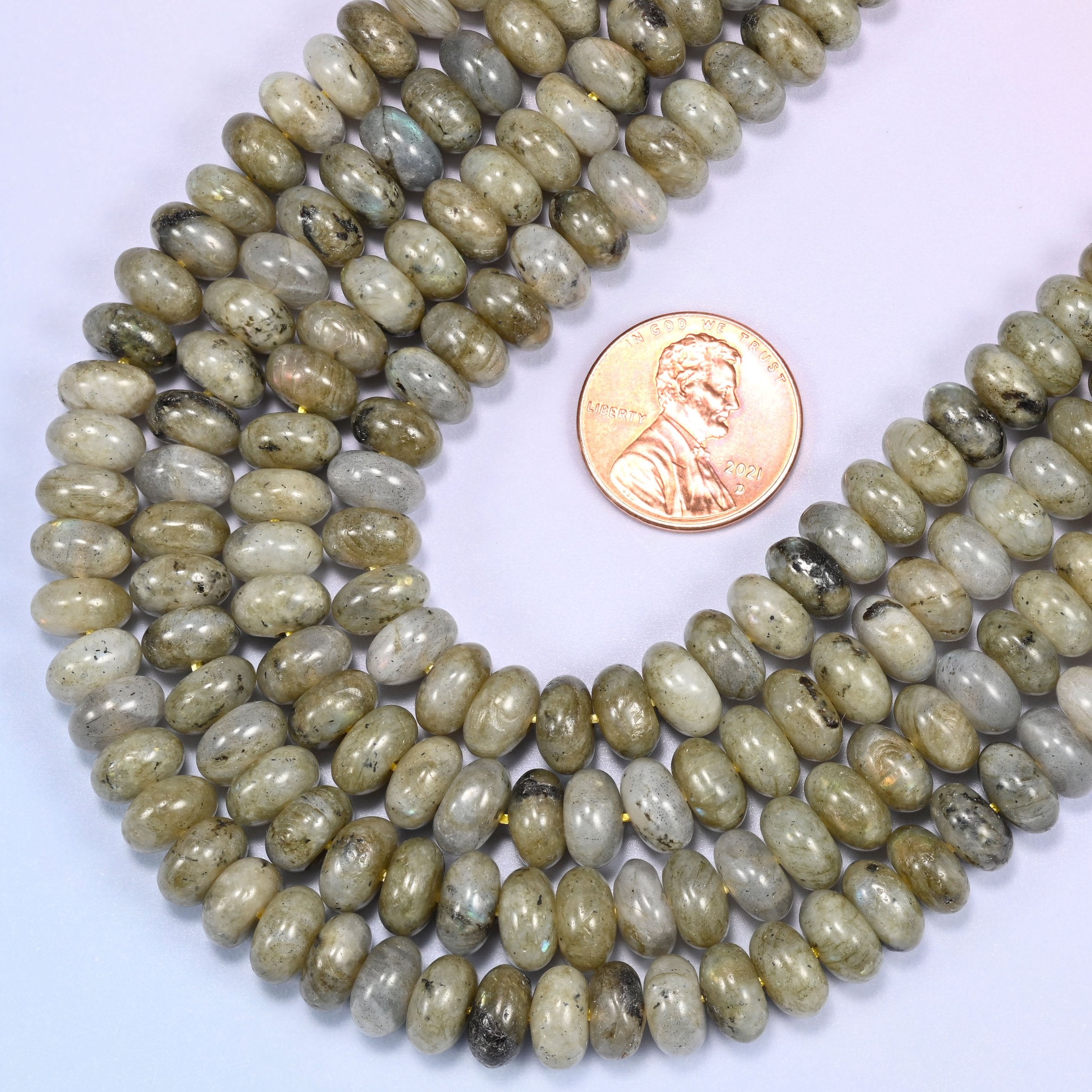 Circular coil of Grey Labradorite bead strands on a lavender background with a penny in the center for size comparison.