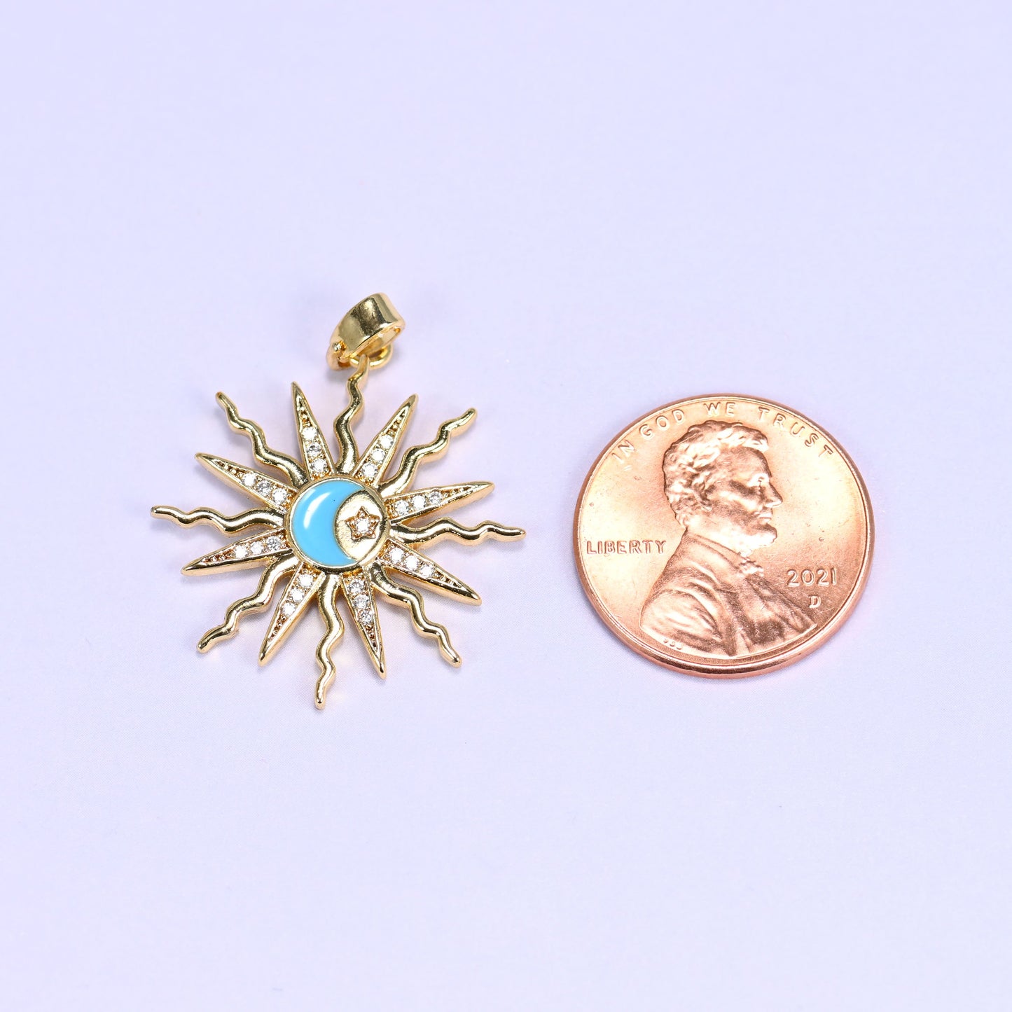 Enamel moon sun zirconia charm scale shot, the blue enamel sunburst pendant photographed next to a US penny.