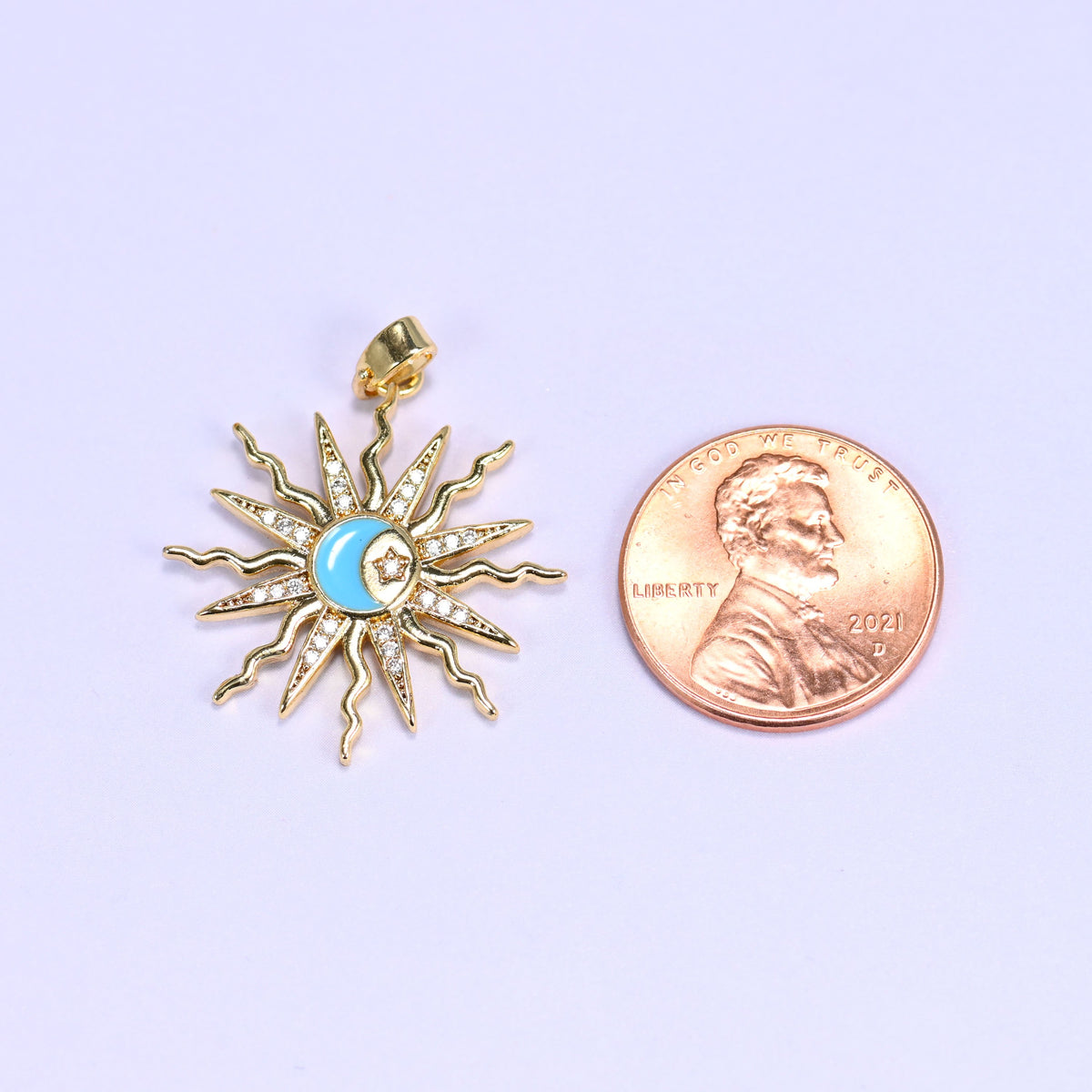 Enamel moon sun zirconia charm scale shot, the blue enamel sunburst pendant photographed next to a US penny.