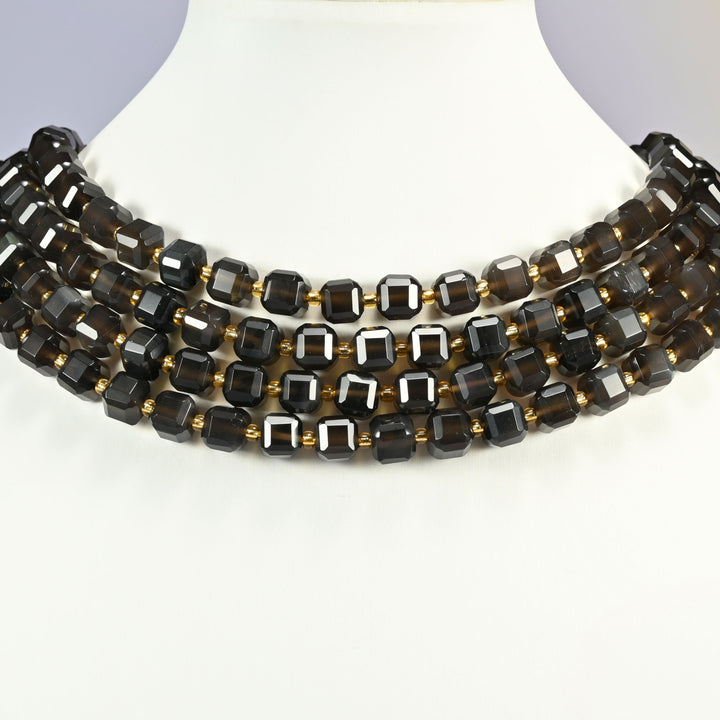 Ice obsidian faceted cube strands layered as a collar on a white display bust, translucent dark brown cubes with gold spacers