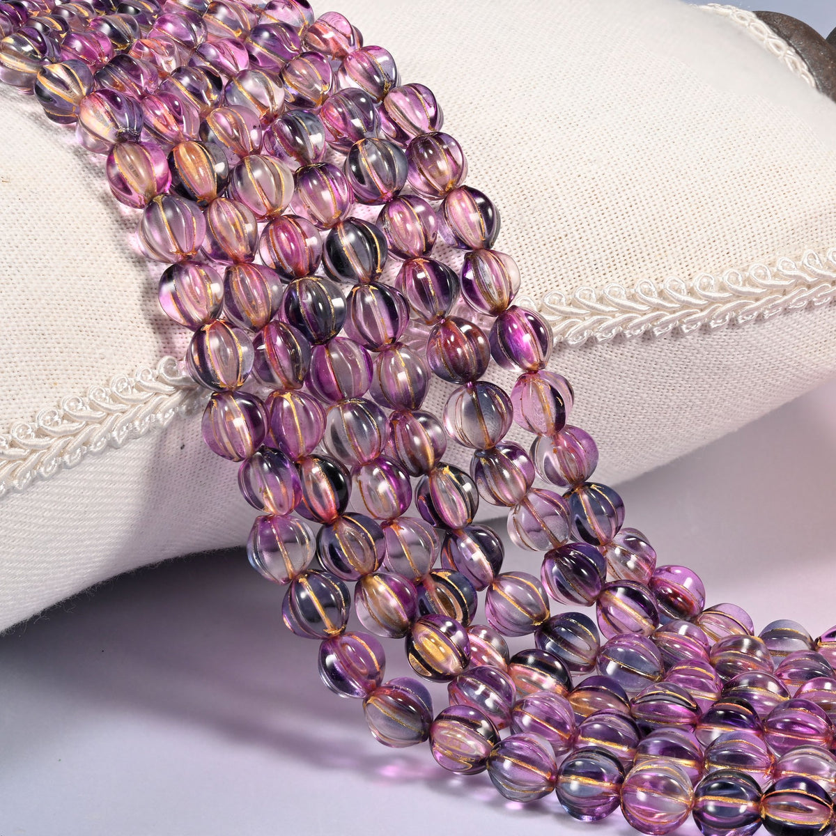 Pink blue gold pumpkin glass beads, 8mm fluted melon rounds, several strands draped forward in rows.