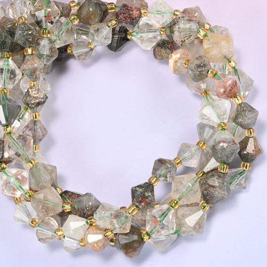 Green Phantom Quartz faceted bicone beads, 8mm and 10mm, coiled into a circle on a light lavender background, showing the natural stone color variation.