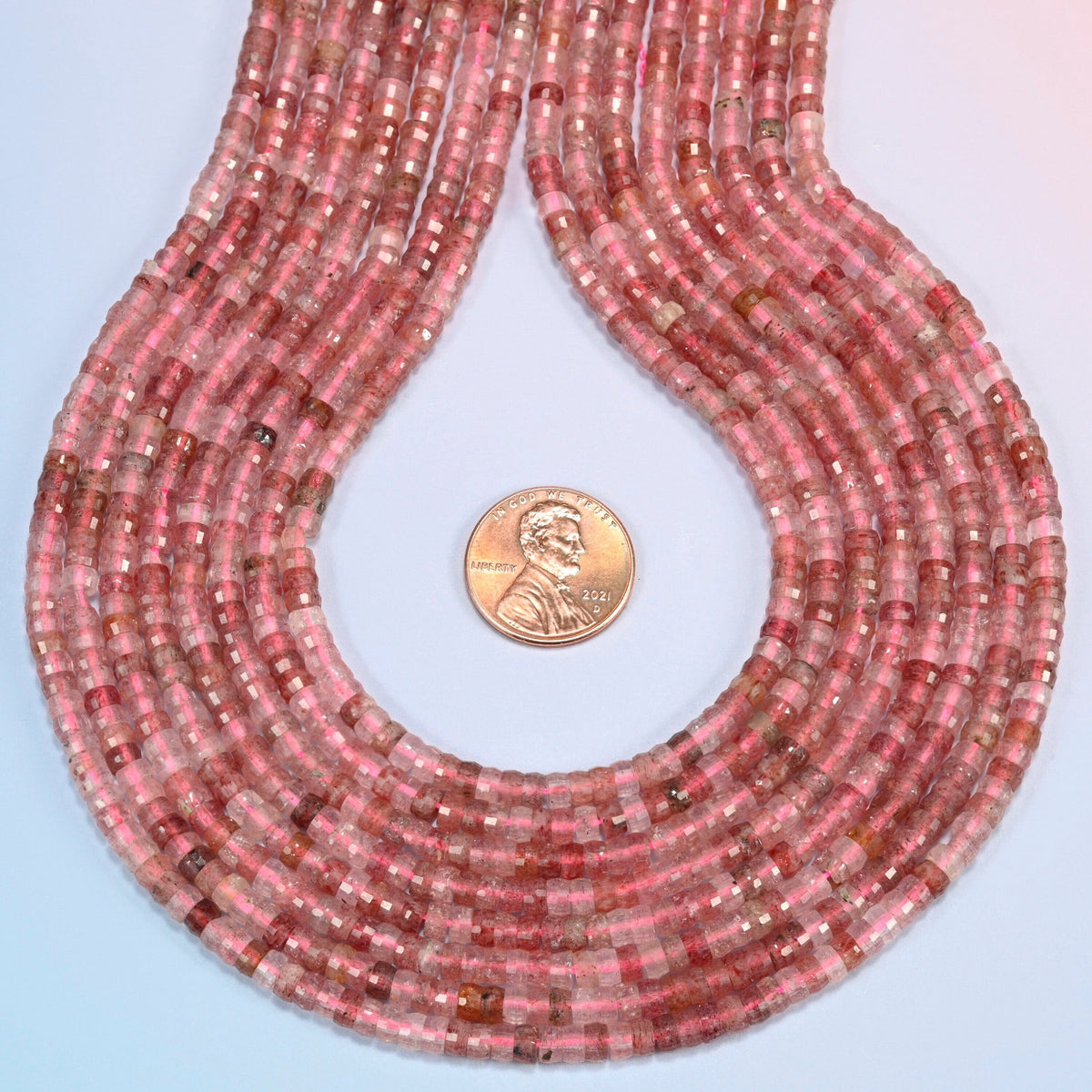 Strawberry quartz faceted heishi disc strands formed into a teardrop loop around a US penny for scale