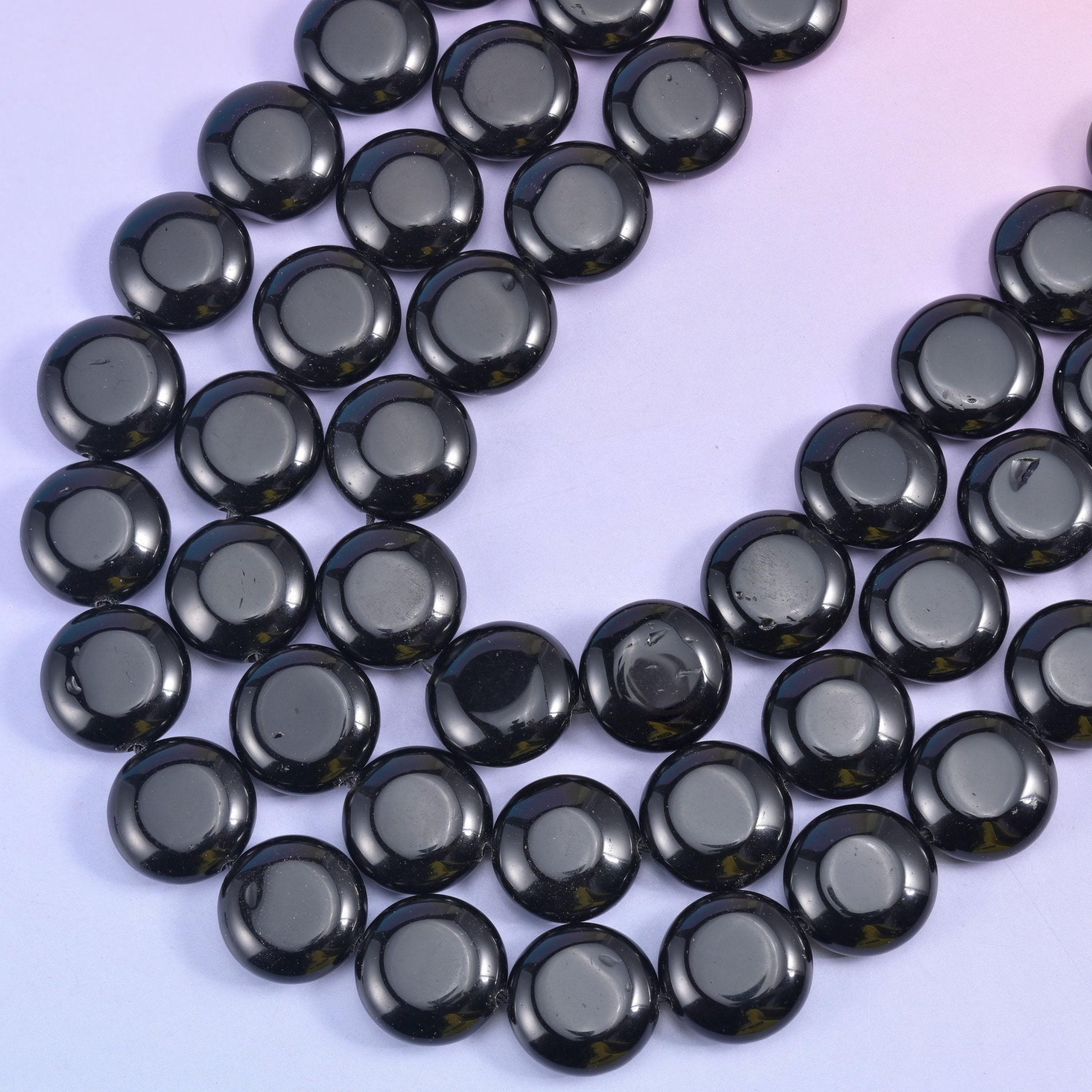 Two rows of black coin beads curving across the frame, drilled through the centre and strung on cord