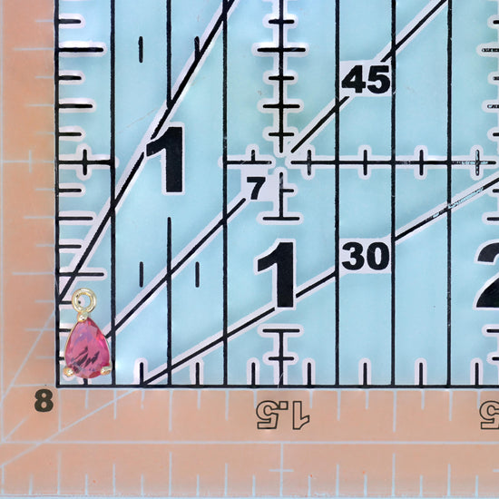 Teardrop zirconia charm in pink placed on a quilting ruler for scale.