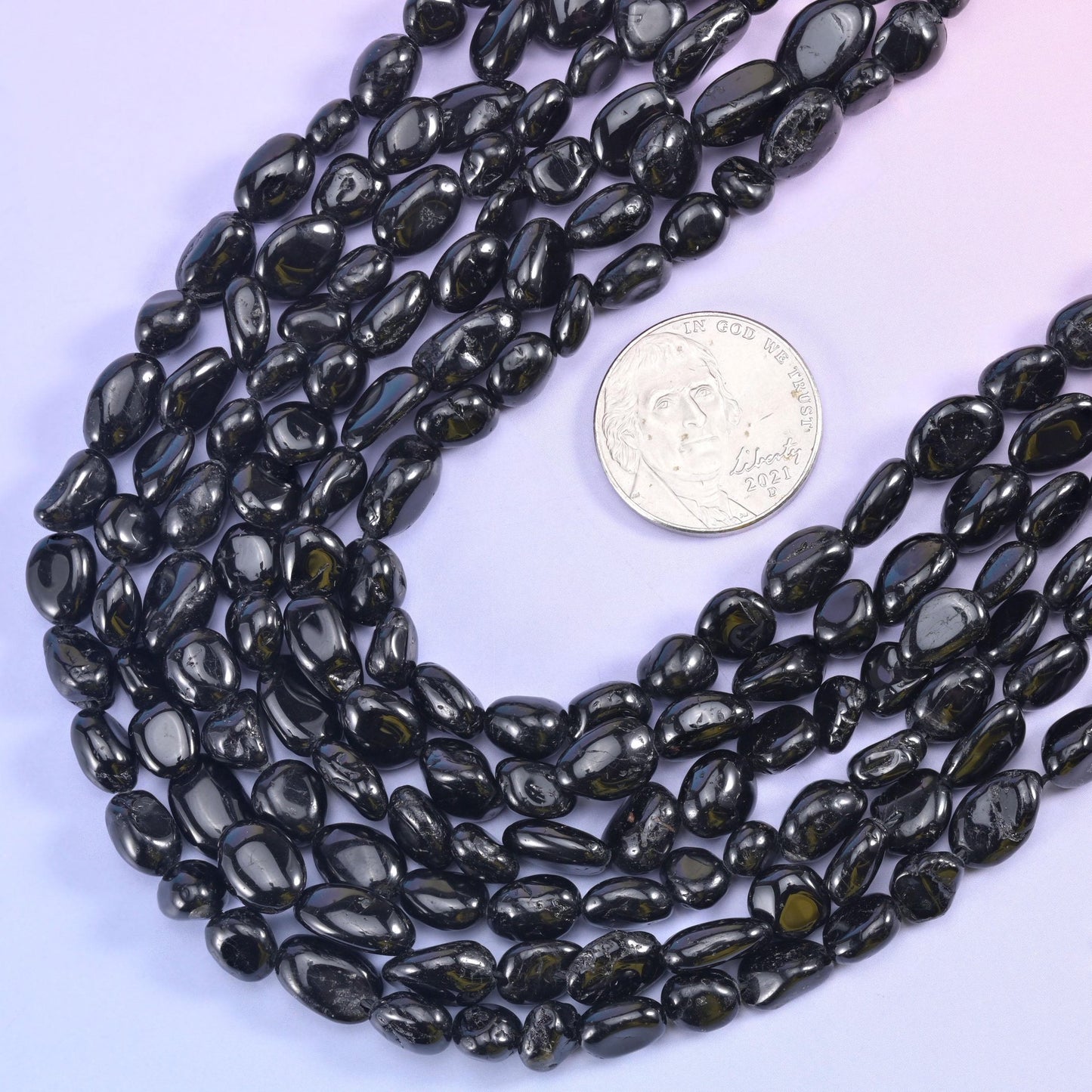 Black tourmaline nugget strands looped around a silver US coin for scale