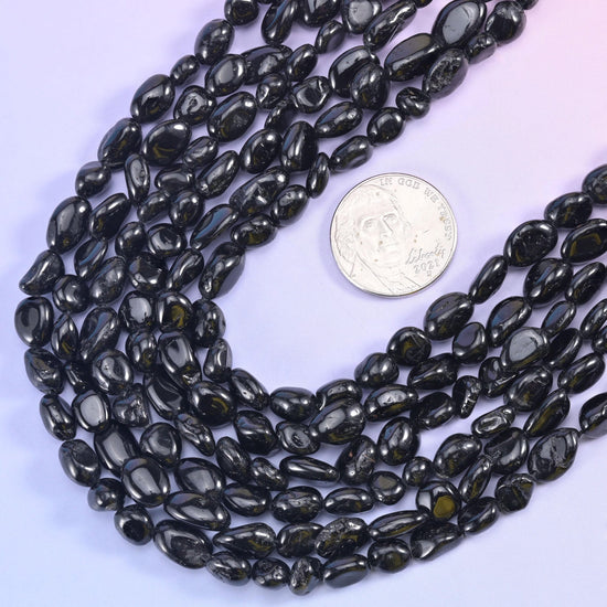 Black tourmaline nugget strands looped around a silver US coin for scale