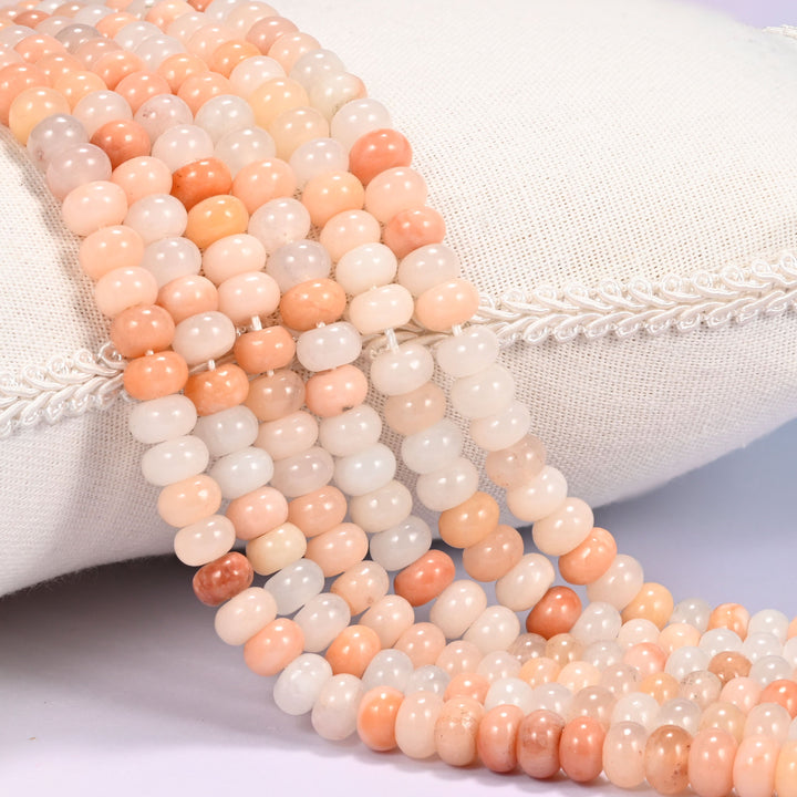 Close-up of multiple strands of polished Pink Aventurine rondelle beads in blush and peach tones, draped over a cream fabric jewelry display bust.