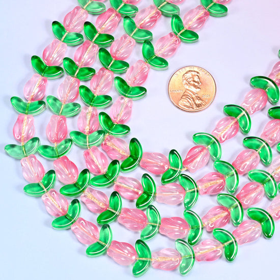 Close-up of pink tulip and green leaf glass beads arranged in a dense coiled cluster on a lavender surface.