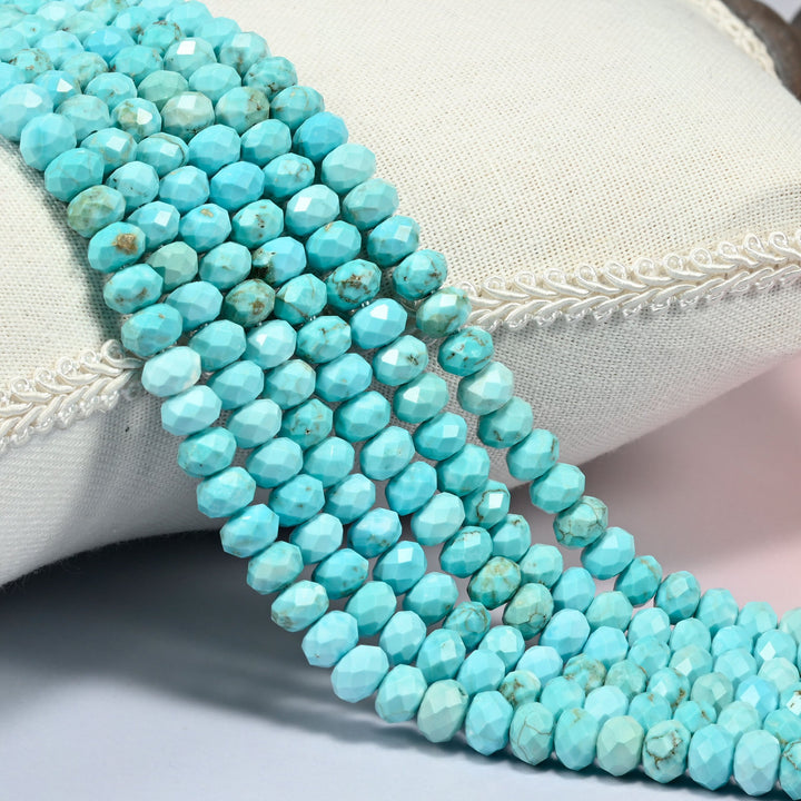 Dyed light blue howlite faceted rondelle beads 5x8mm in robin's egg turquoise with brown veining, strands draped over a white cushion