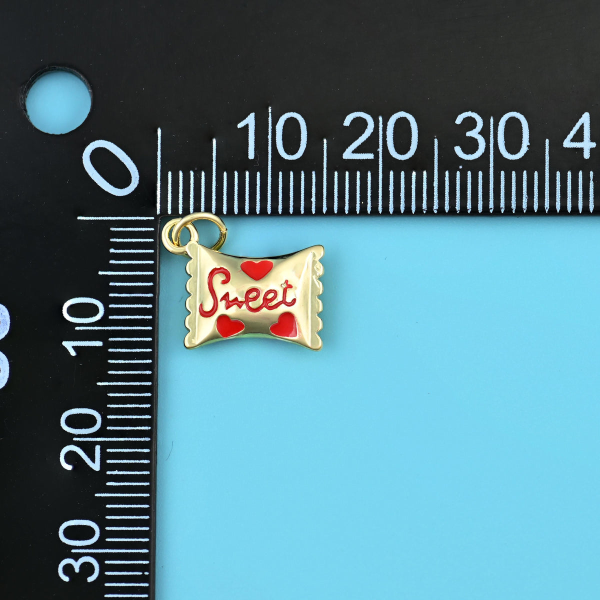 16mm enamel sweet candy charm on a millimetre ruler, red script and hearts on polished gold.