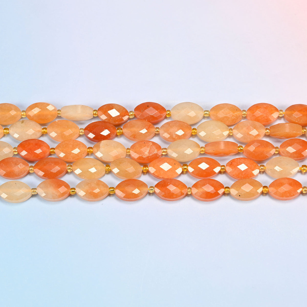 Several strands of red aventurine faceted flat oval beads laid in straight rows with gold seed bead spacers