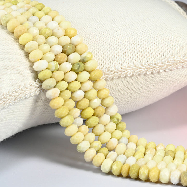 Butter jade faceted rondelle beads over a white cushion, soft yellow stone with white beads mixed in.