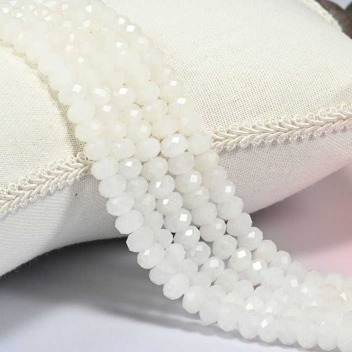 White jade faceted rondelle beads 5x8mm in soft milky white, several strands draped over a white cushion
