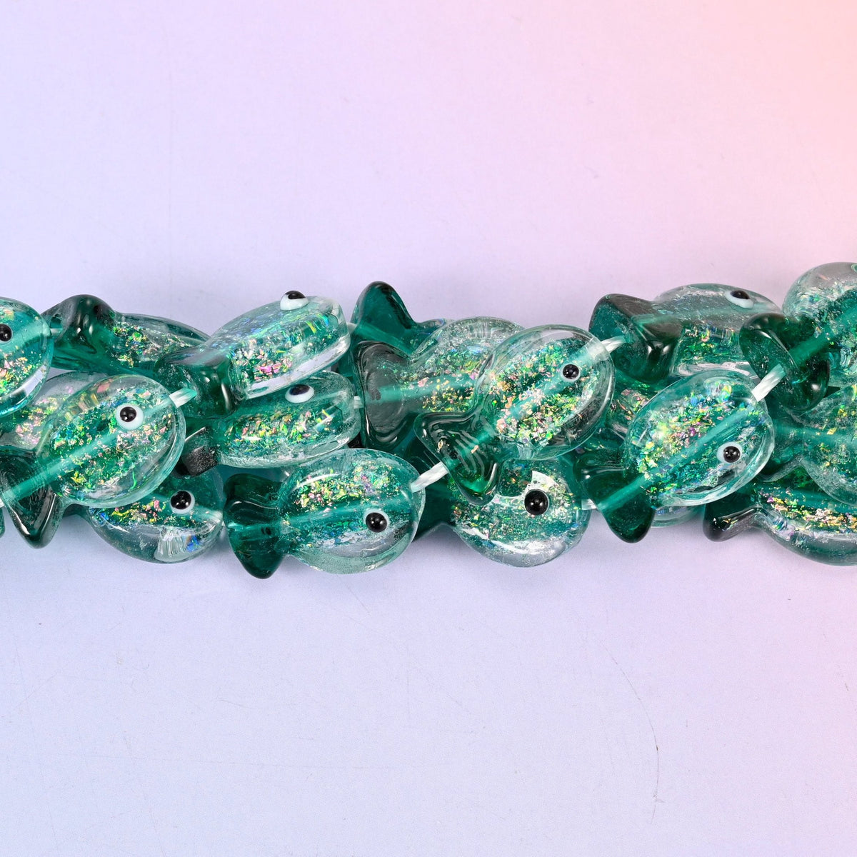 Iridescent Green Fish Glass Beads — sea green lampwork fish, translucent at the belly and deeper at the fins, with gold glitter drifting through the glass and a black dot eye on each side.