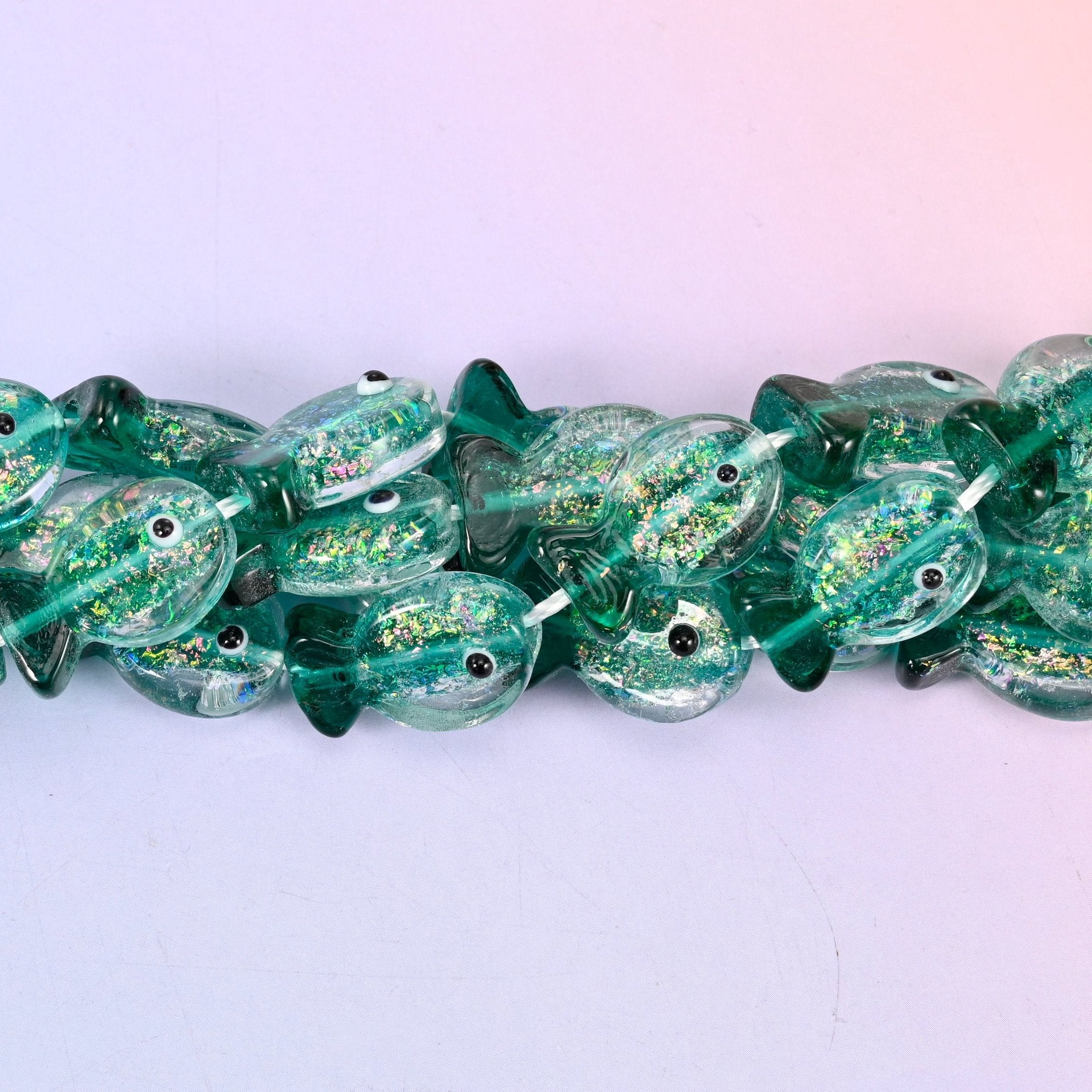 Iridescent Green Fish Glass Beads — sea green lampwork fish, translucent at the belly and deeper at the fins, with gold glitter drifting through the glass and a black dot eye on each side.