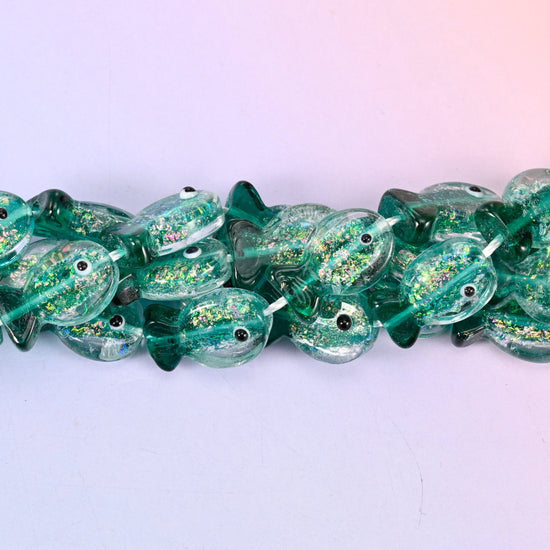 Iridescent Green Fish Glass Beads — sea green lampwork fish, translucent at the belly and deeper at the fins, with gold glitter drifting through the glass and a black dot eye on each side.