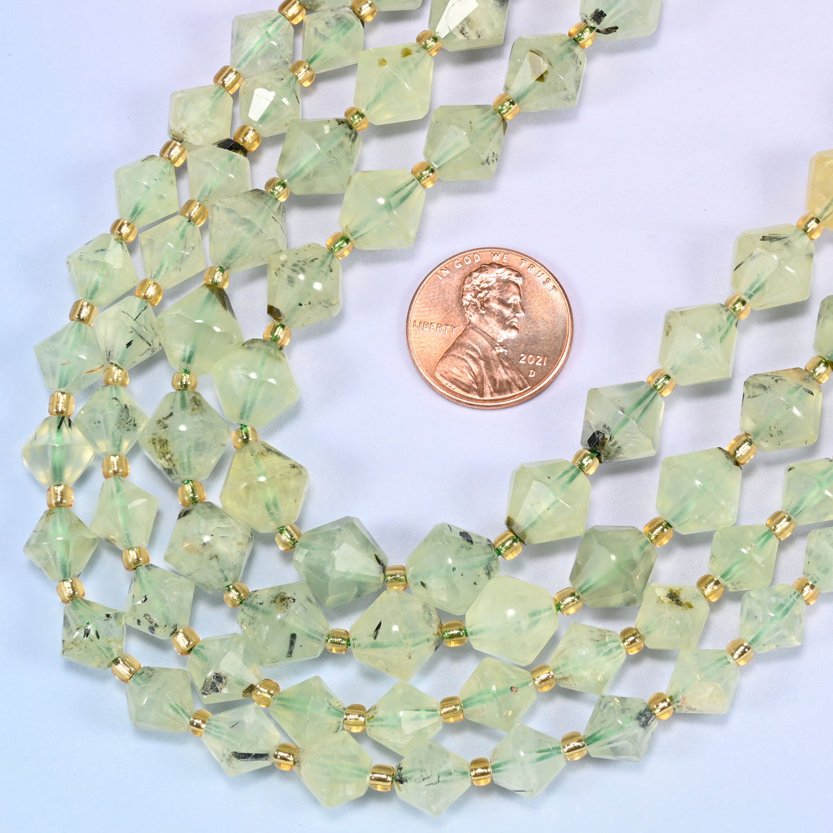 Close-up of Green Prehnite faceted bicone beads, 8mm and 10mm, in a loose curved loop, showing the faceted cut and gold-tone spacer beads.