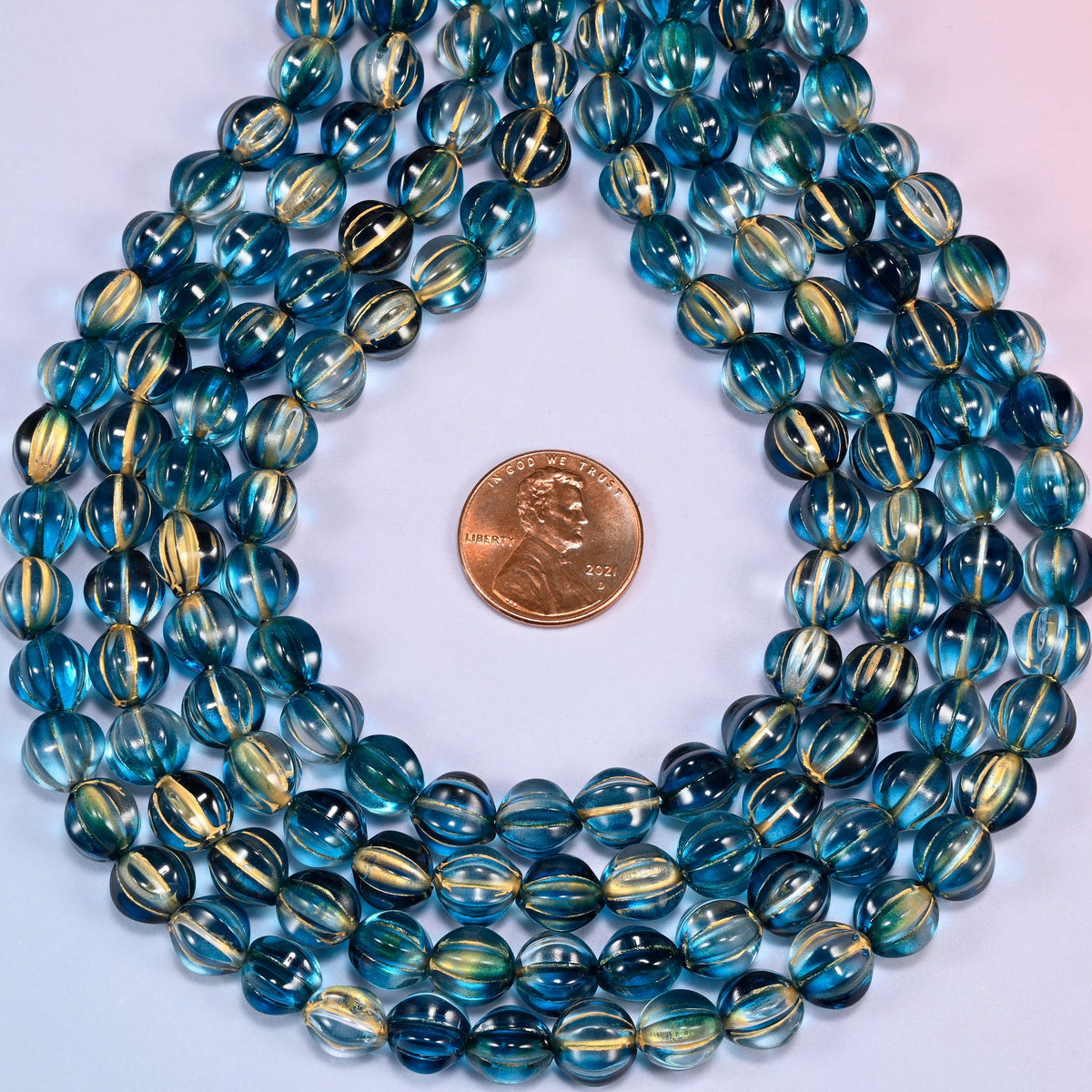 Dark blue gold pumpkin glass beads coiled into a ring, shown with a US penny in the open center for scale.