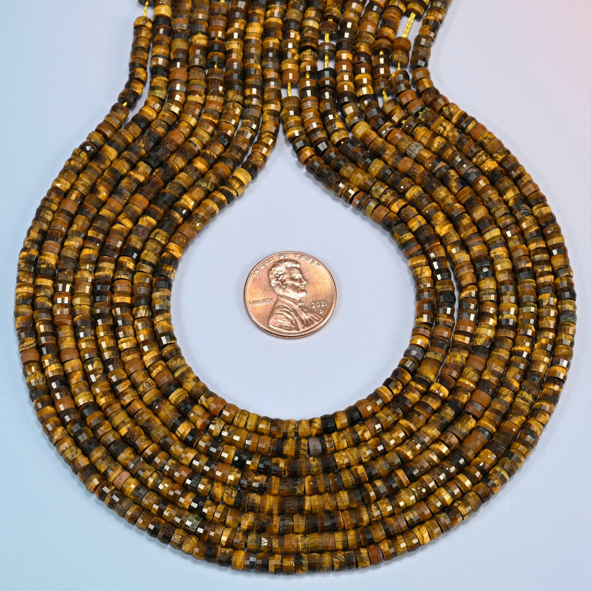 Tiger eye faceted heishi disc strands formed into a teardrop loop around a US penny for scale