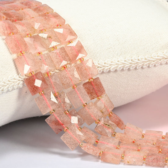 Natural strawberry quartz faceted flat square beads 10x10mm with small gold seed bead spacers, several strands draped over a white cushion